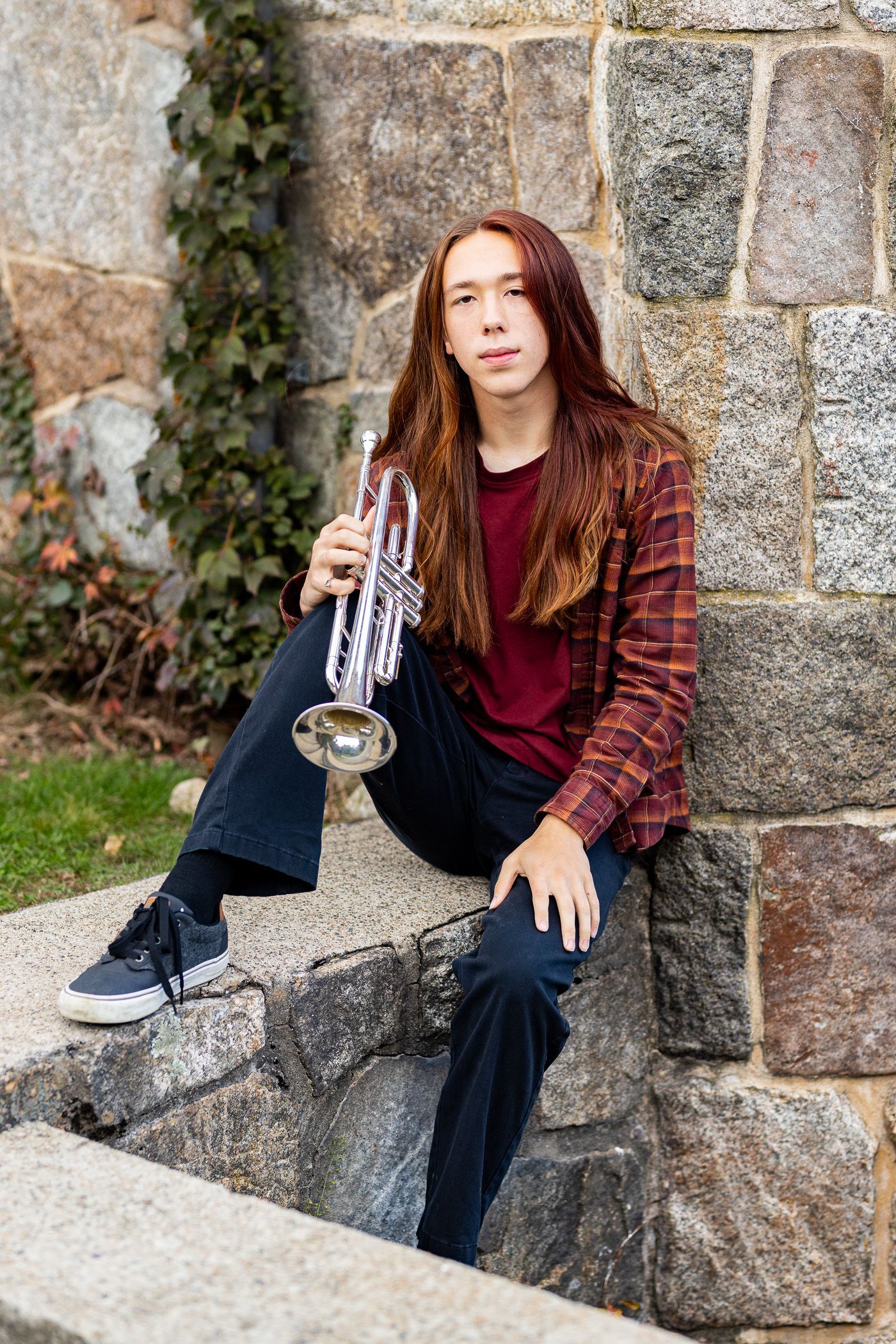 A young man is sitting on a stone wall holding a trumpet.