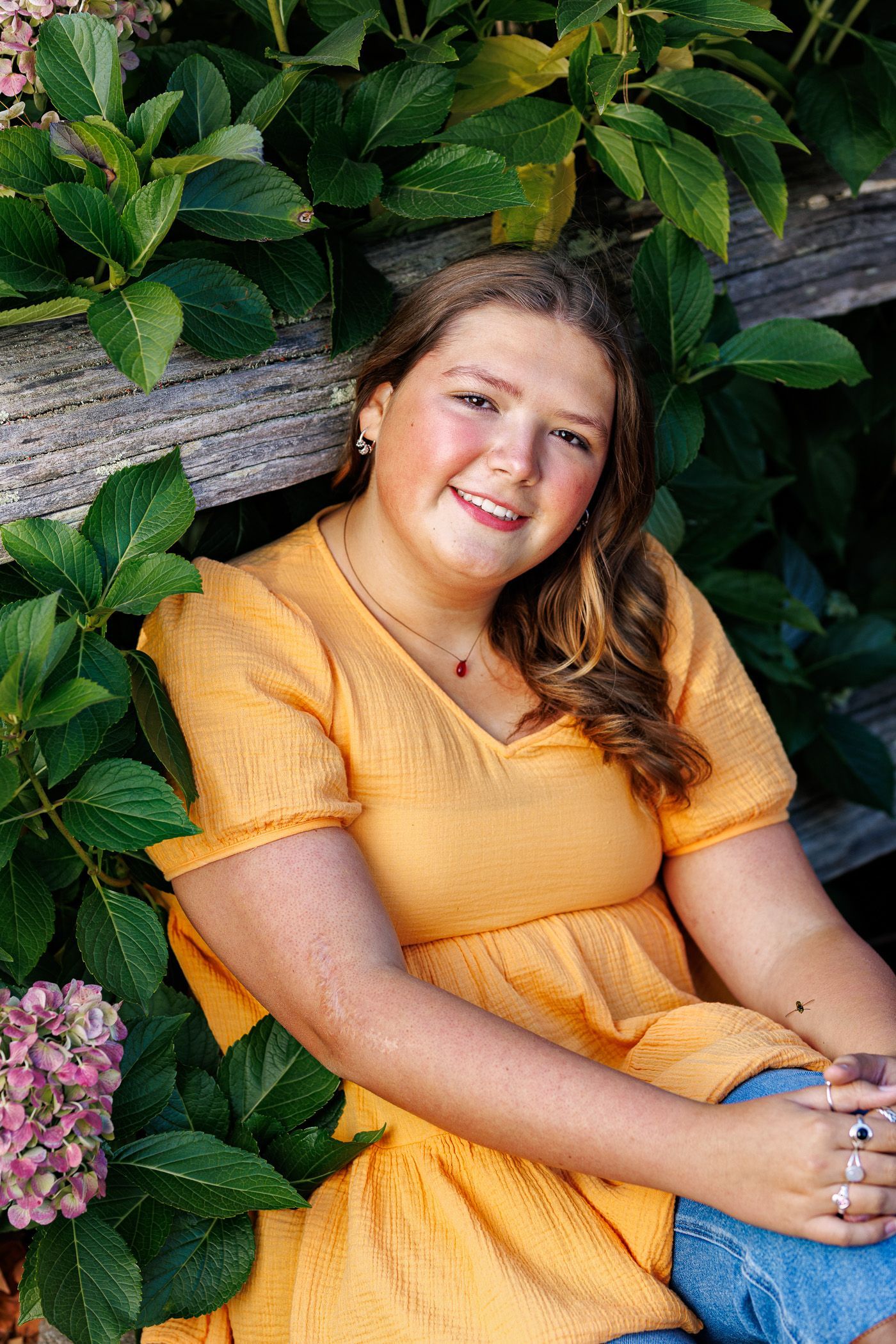 Photography MA -A young girl in a yellow dress is sitting in front of a bush.