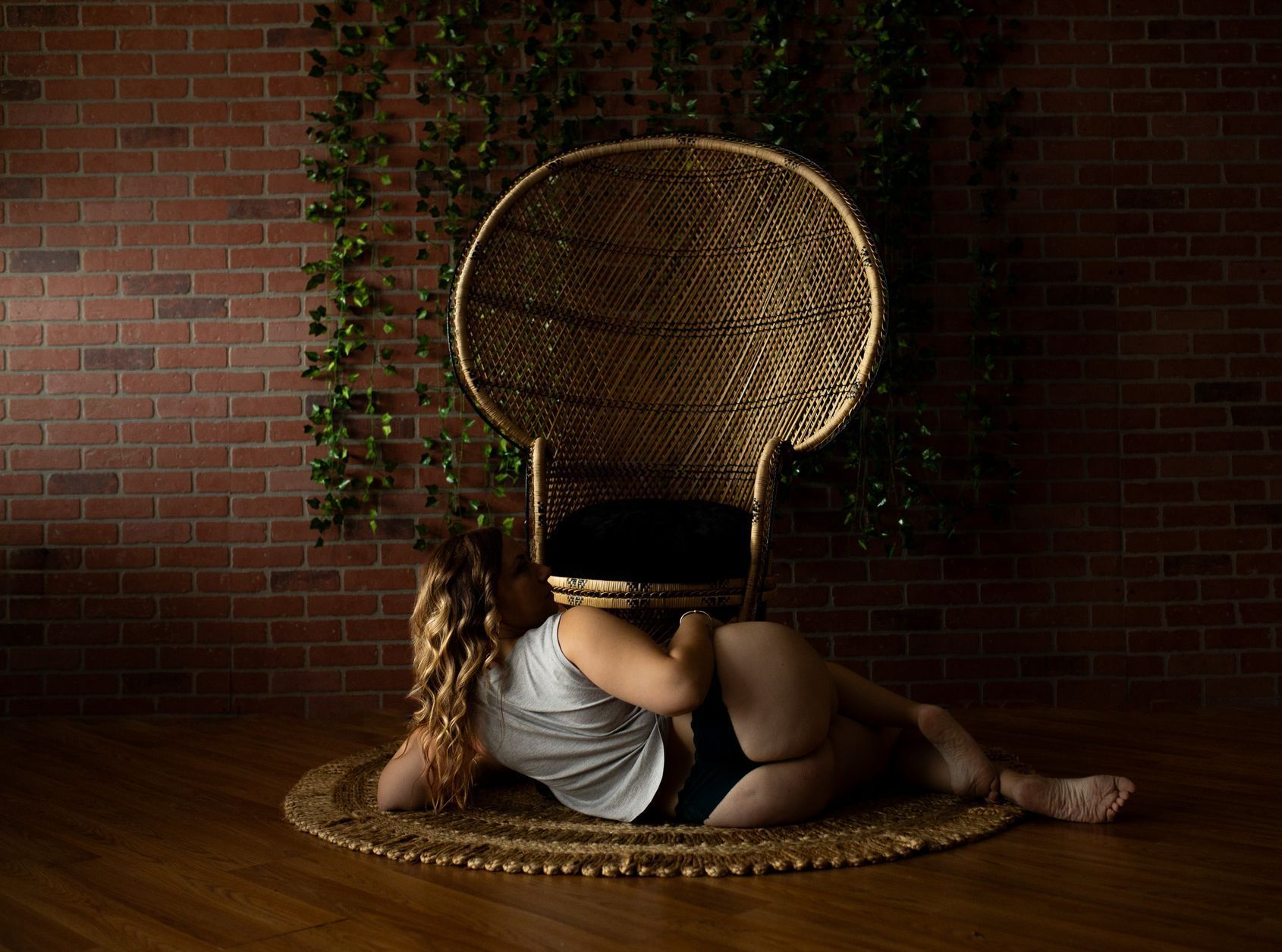 A woman is laying on the floor next to a wicker chair.