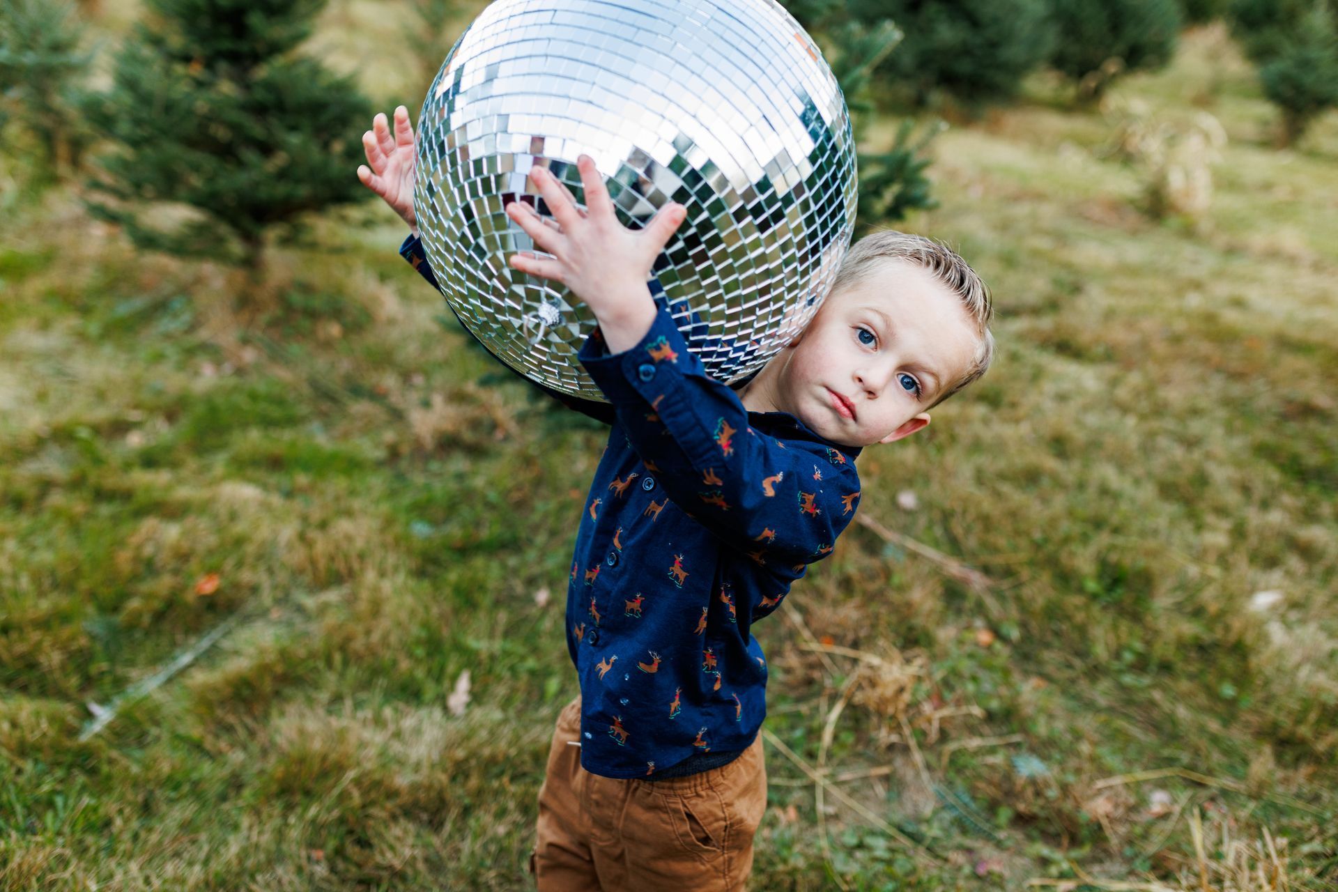 A young boy is holding a large disco ball on his shoulders.