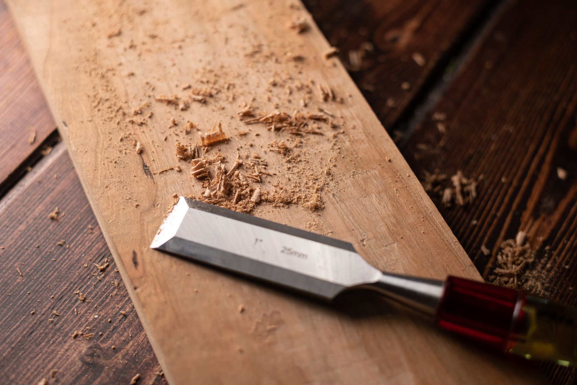 A chisel is sitting on top of a piece of wood on a wooden table.
