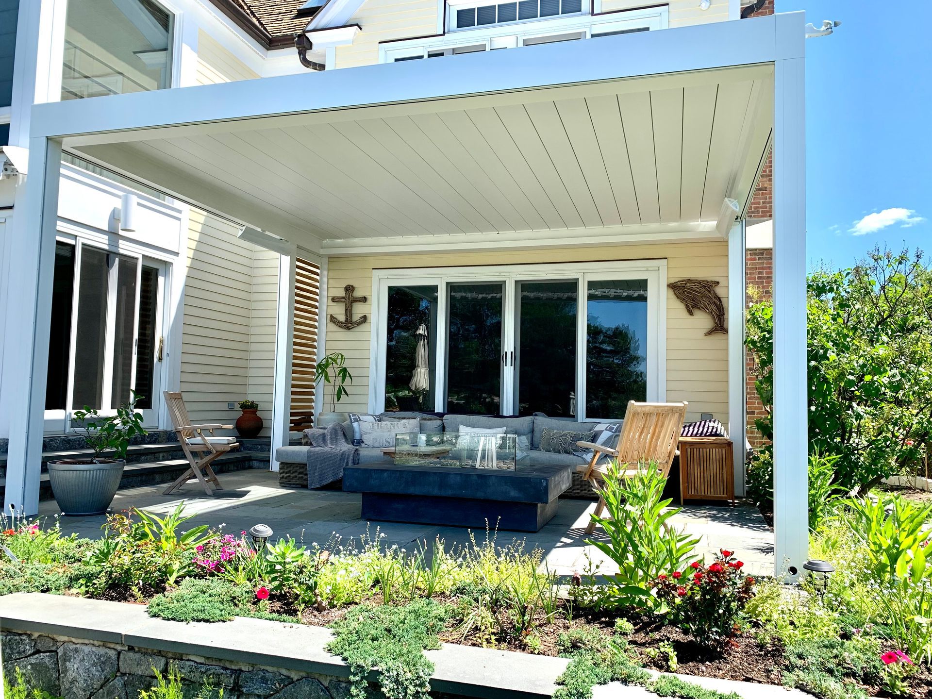 A patio with a pergola and a couch and chairs in front of a house.