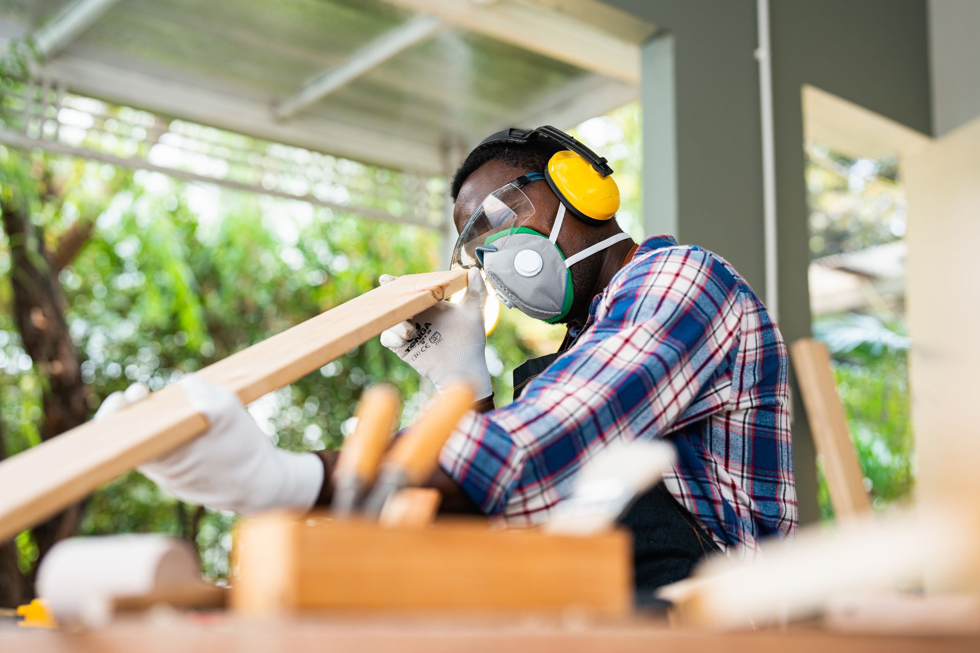 A man wearing a mask and ear muffs is cutting a piece of wood.