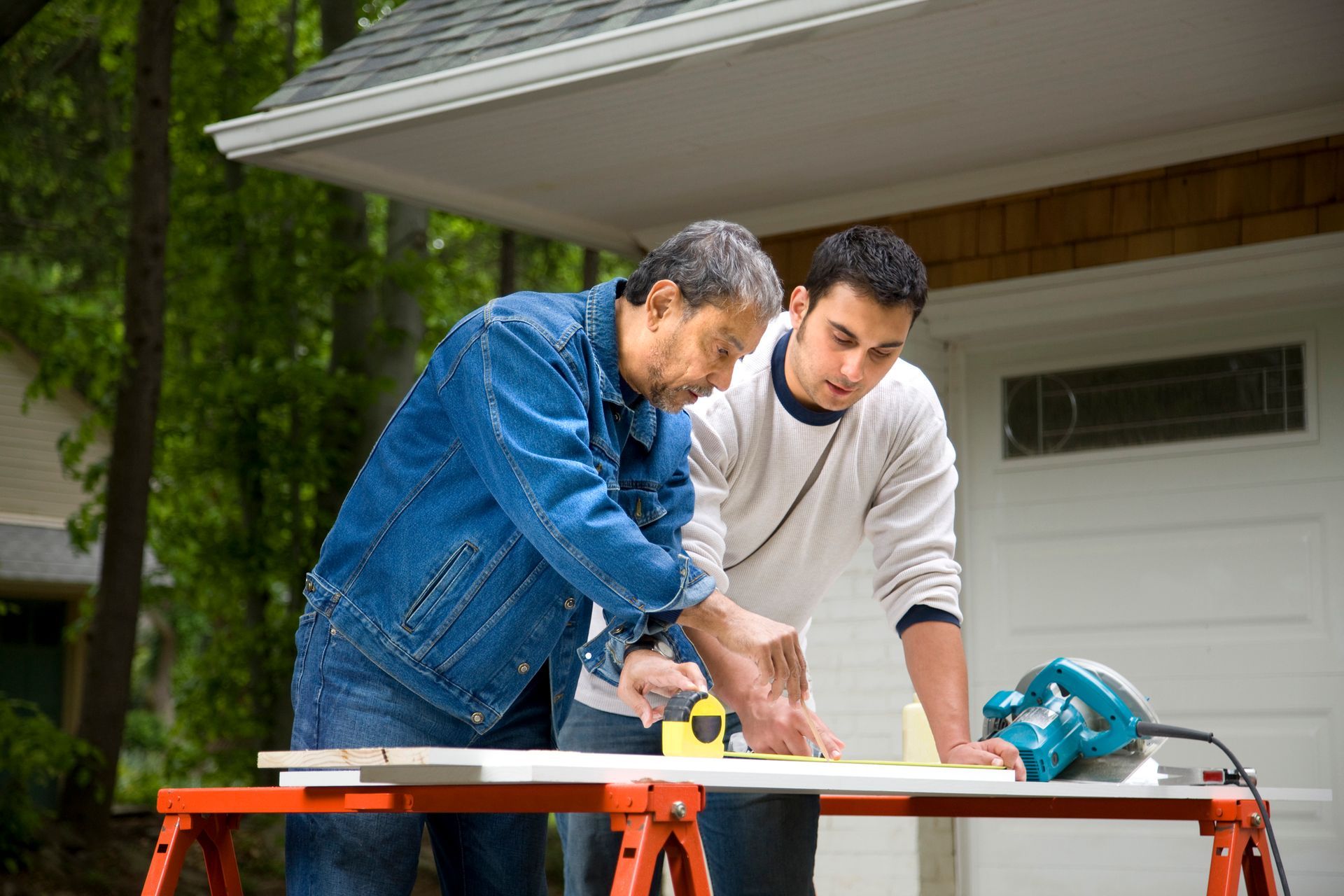 Two men are working on a table outside of a house.