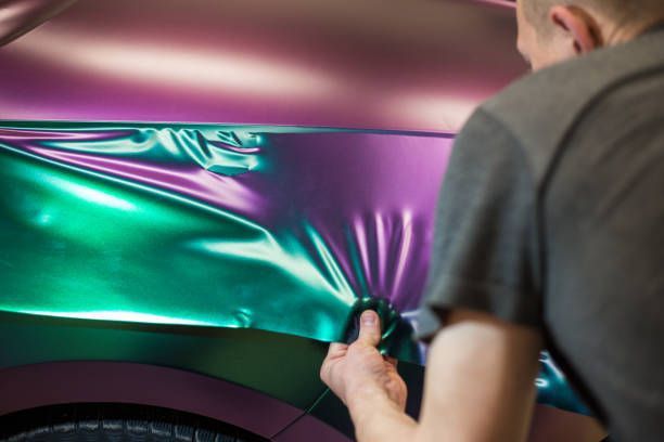 A man is wrapping a car in purple and green foil.