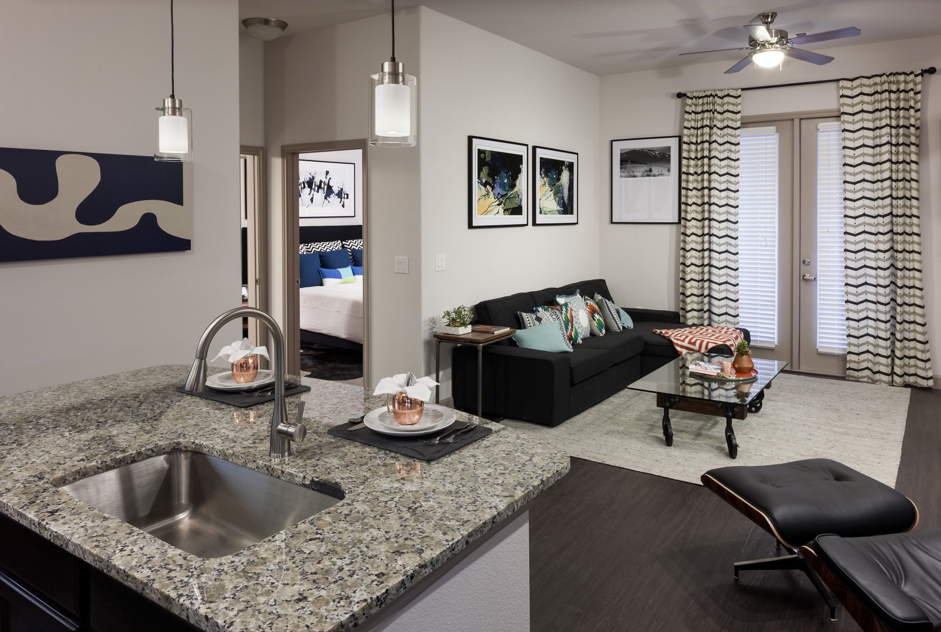 Open-concept living area with granite kitchen island, sink, and a black sofa; doorway to a bedroom.