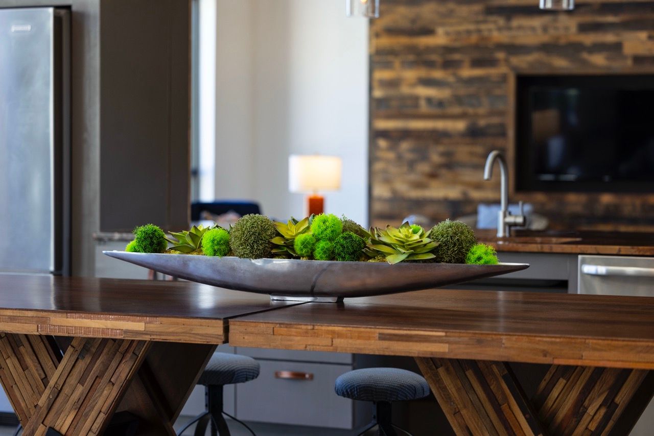 Modern apartment kitchen with a wooden dining table and a green plant centerpiece.