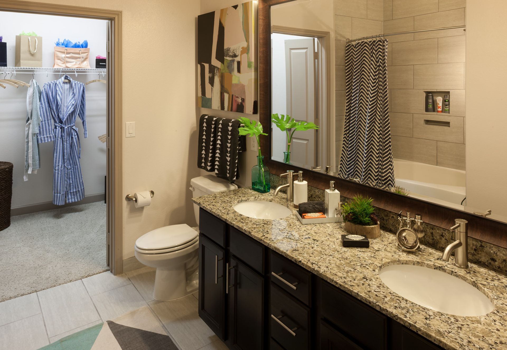 Double-sink bathroom with granite countertop, large mirror, and an open closet with clothes.