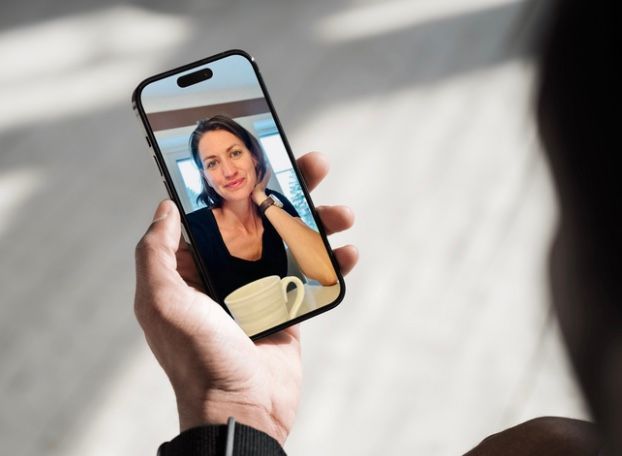 Person holder telefonen under videosamtale med smilende kvinne som holder et krus.