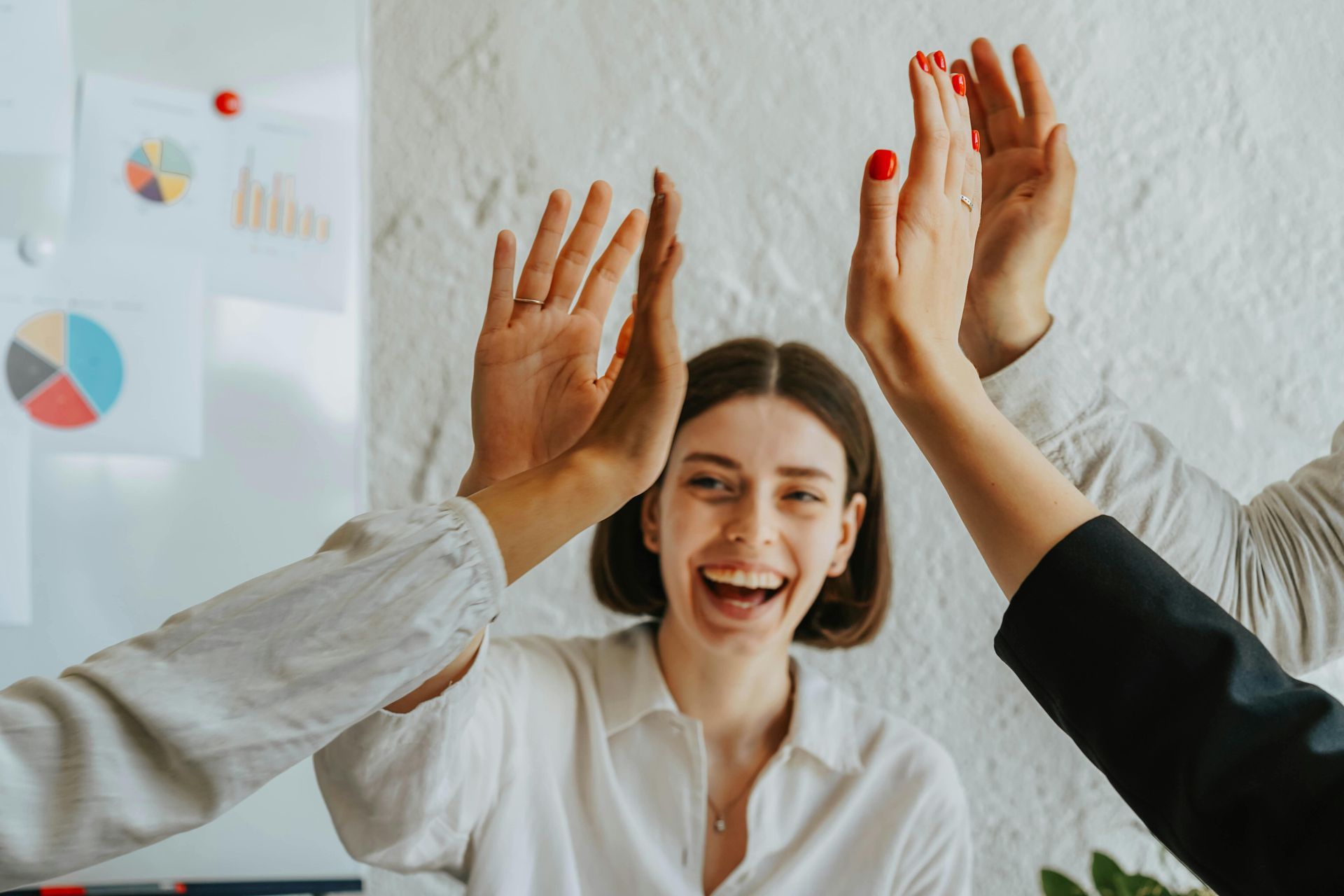 Woman laughing, high-fiving with colleagues in an office setting, celebrating success.
