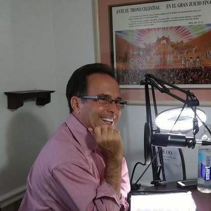 A man in a pink shirt is smiling in front of a microphone