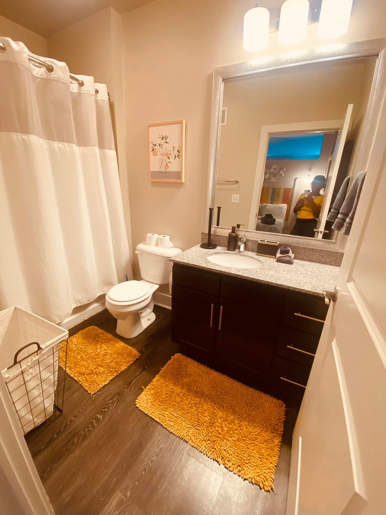 A bathroom with a toilet , sink , mirror and shower curtain.