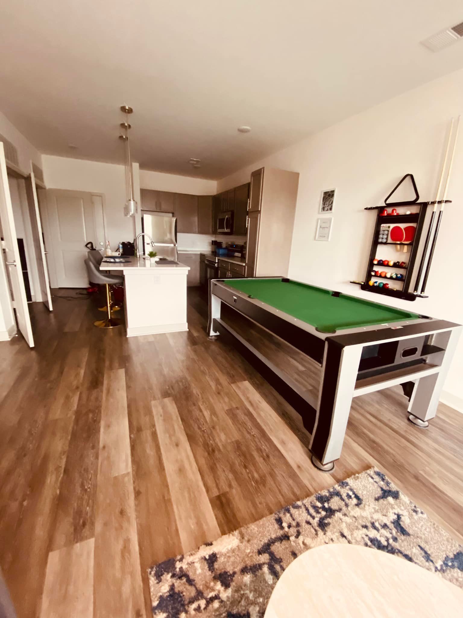 A pool table is sitting in a living room next to a kitchen.