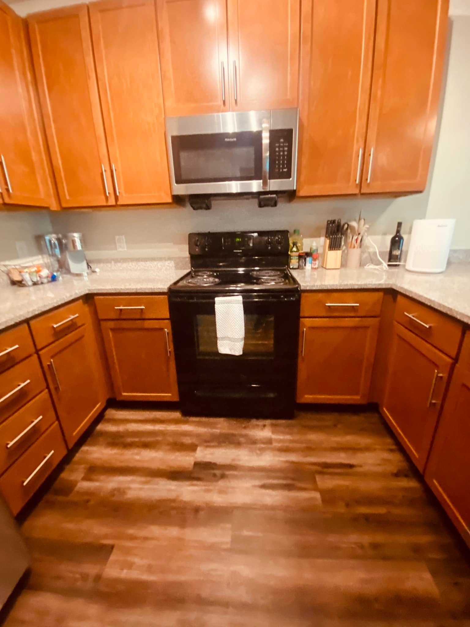 A kitchen with wooden cabinets , stainless steel appliances , a stove and a microwave.