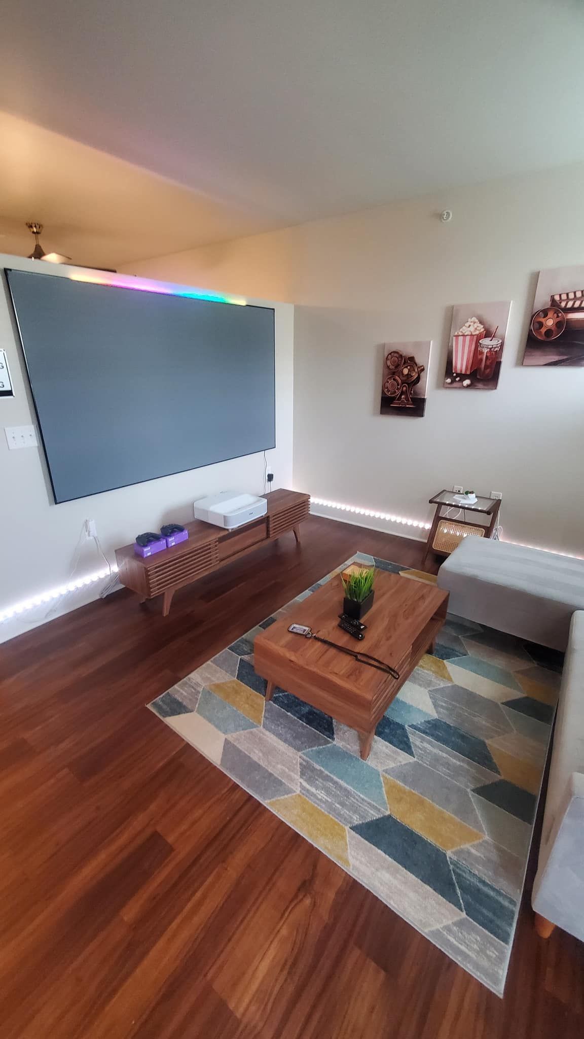 A living room with hardwood floors , a couch , a coffee table , and a projector screen.