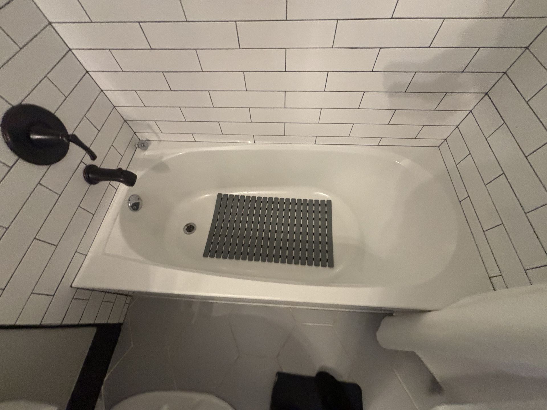 Bathroom with white tub, black faucet, and black anti-slip mat. White subway tile on the walls.