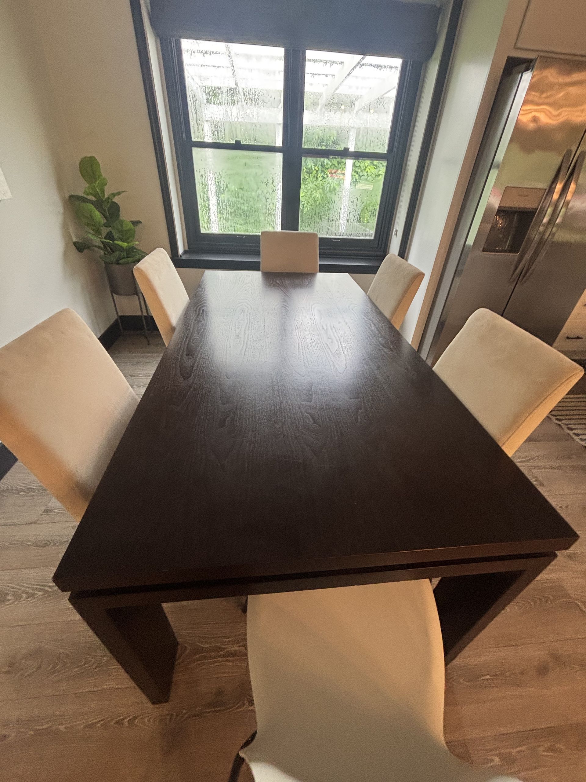 Dark wood dining table with four cream chairs set in front of a window.