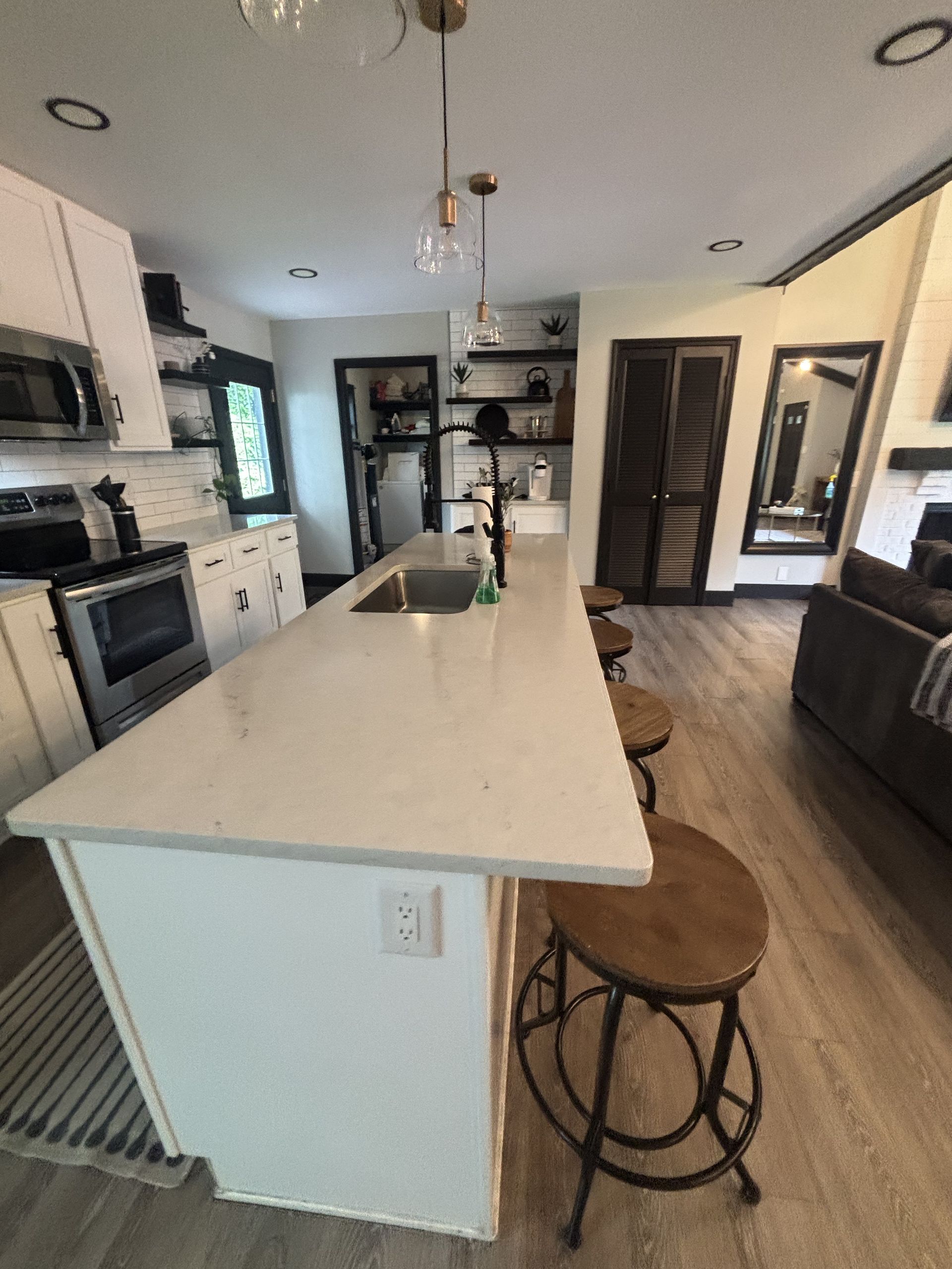 Kitchen with white cabinets, island, and bar stools. Stainless steel appliances. Light wood floors.