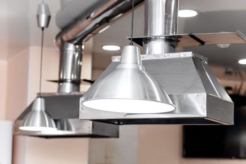 Three silver metal pendant lights and ductwork hanging from a ceiling in an indoor space