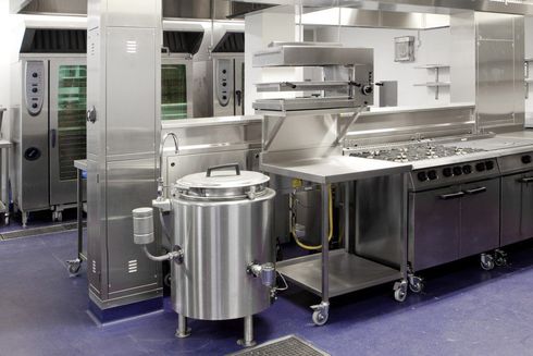 Stainless steel commercial kitchen with ovens, prep tables, and large cooking equipment on wheels