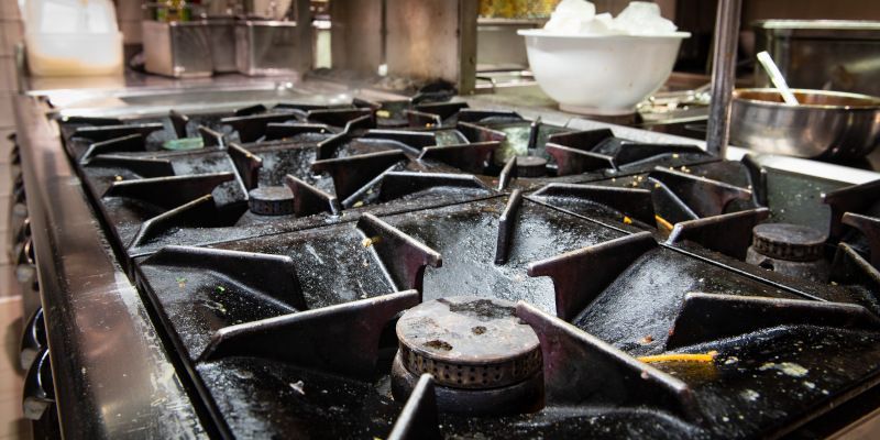 Close-up of a commercial gas stove with multiple black grates and burners in a stainless-steel kitchen.