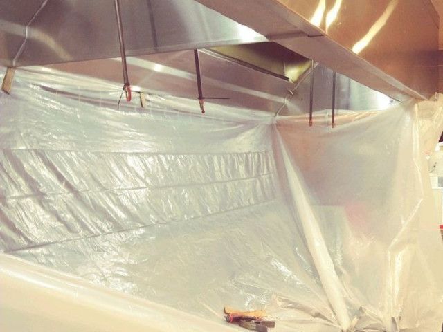 Plastic sheeting covers a room, with exposed ceiling beams and metal ducts overhead.