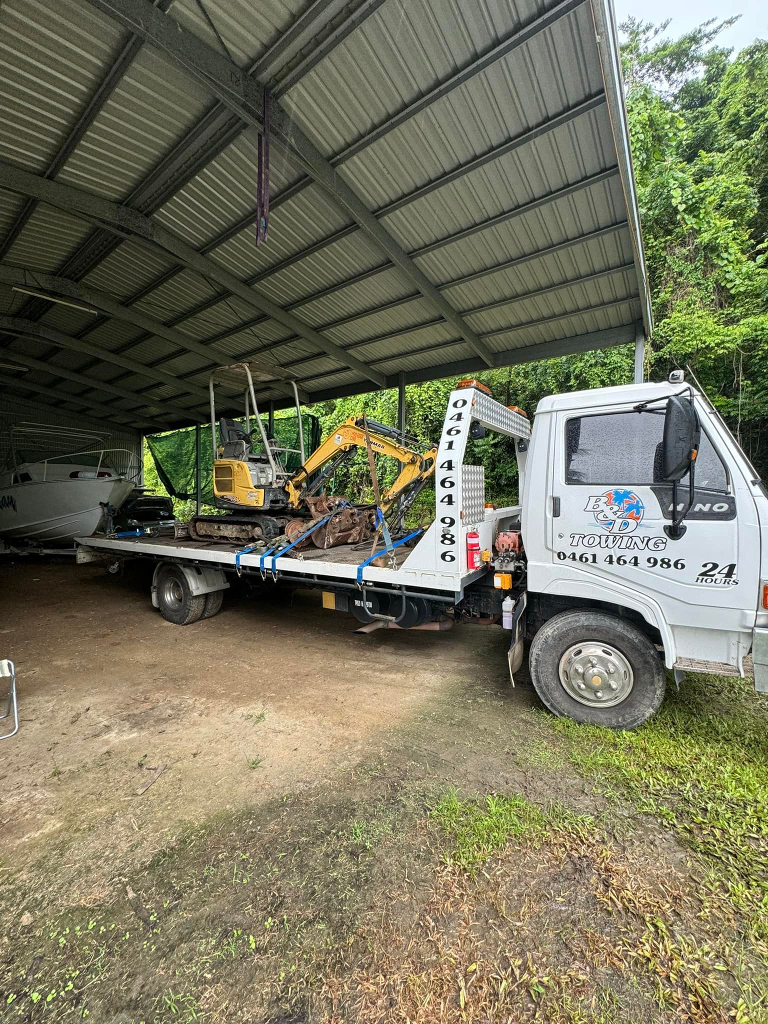 Flatbed Tow Truck With Mini Excavator Under a Metal Roof Shed — B&D Auto Group & Towing in Bowen, QLD