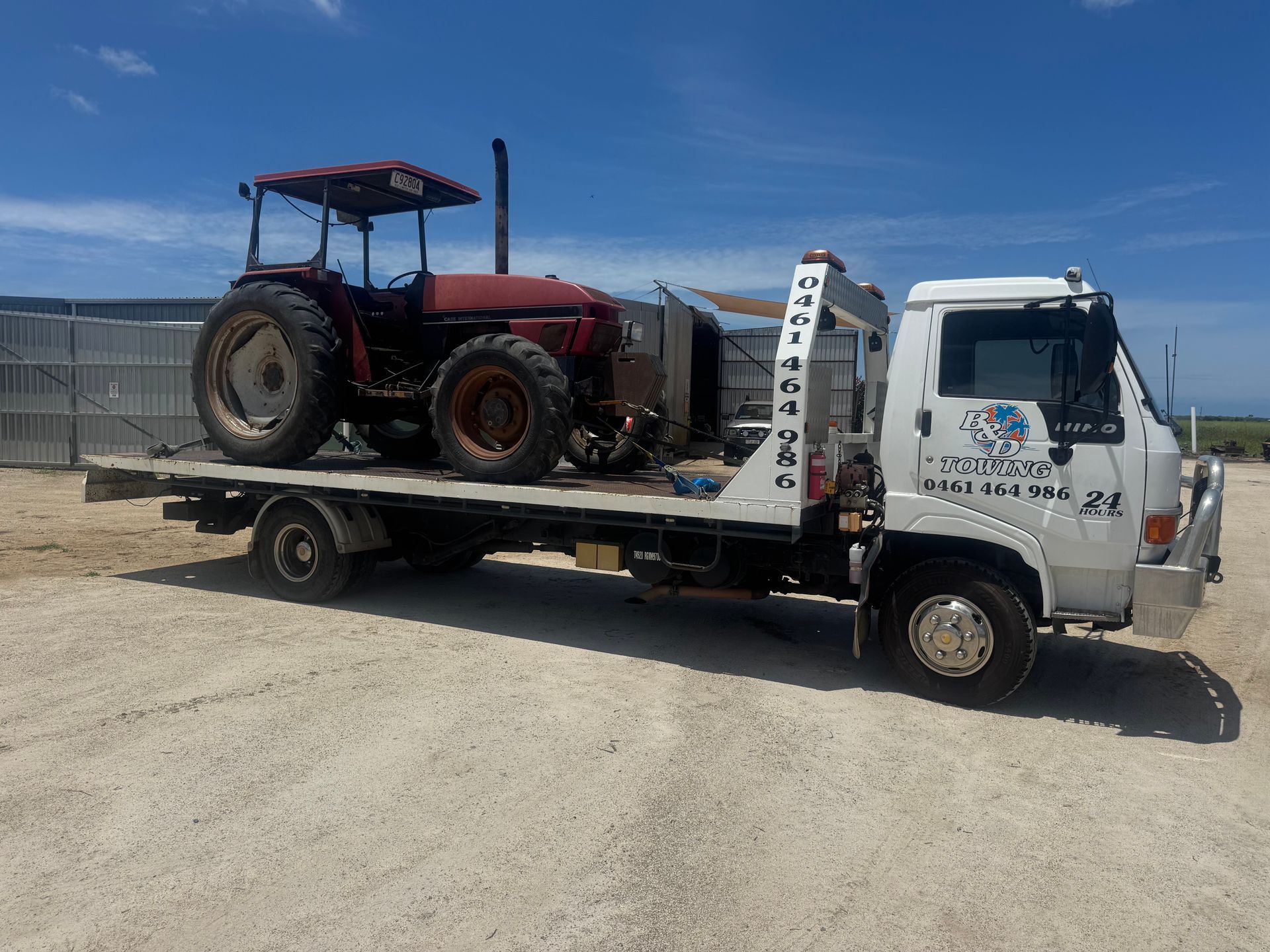 A Red Tractor on a Flatbed Tow Truck on a Gravel Road, Under a Blue Sky — B&D Auto Group & Towing in Bowen, QLD