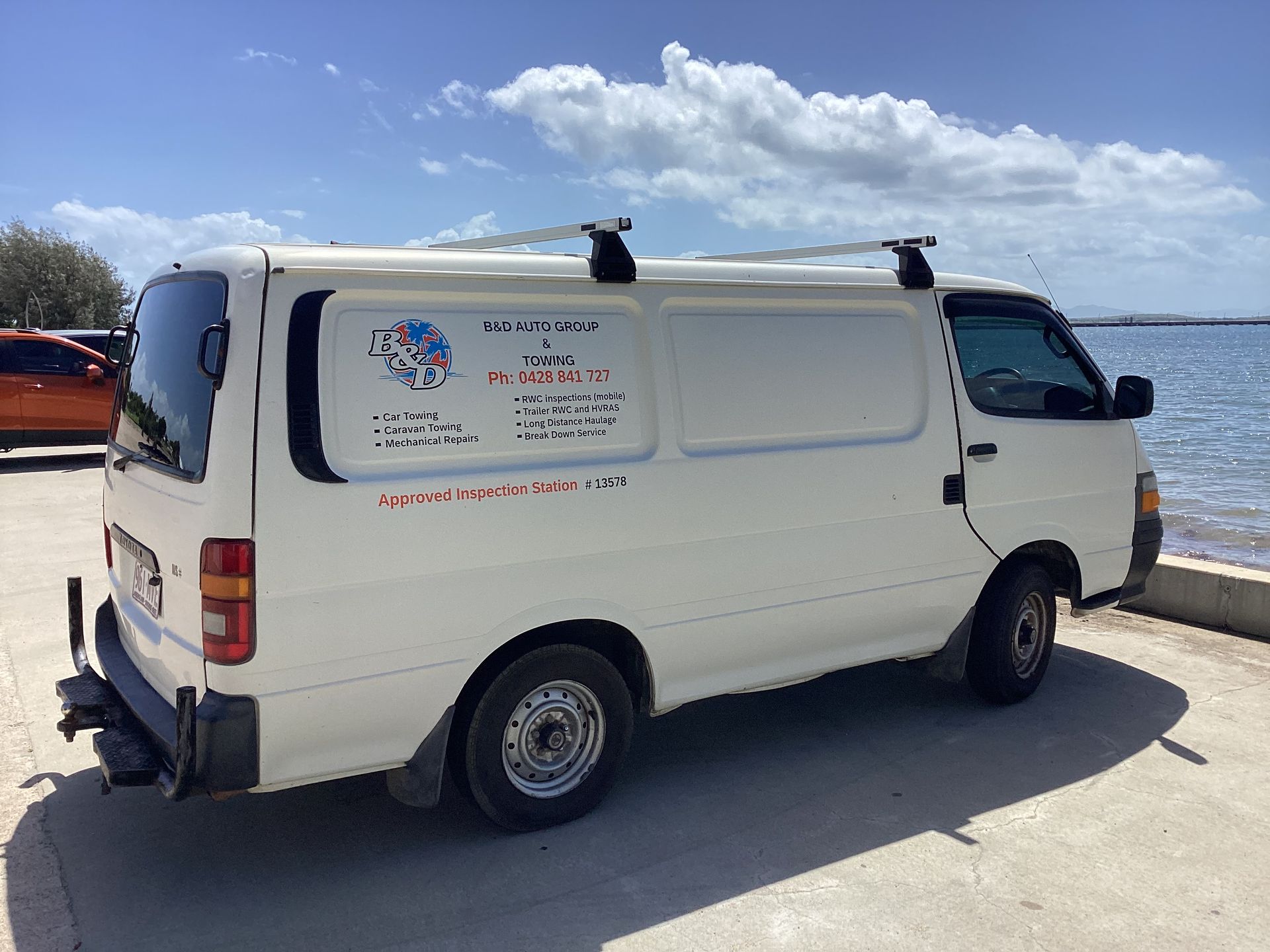 Flatbed Tow Truck Towing a White Caravan on a Paved Surface Under a Cloudy Sky — B&D Auto Group & Towing in Bowen, QLD
