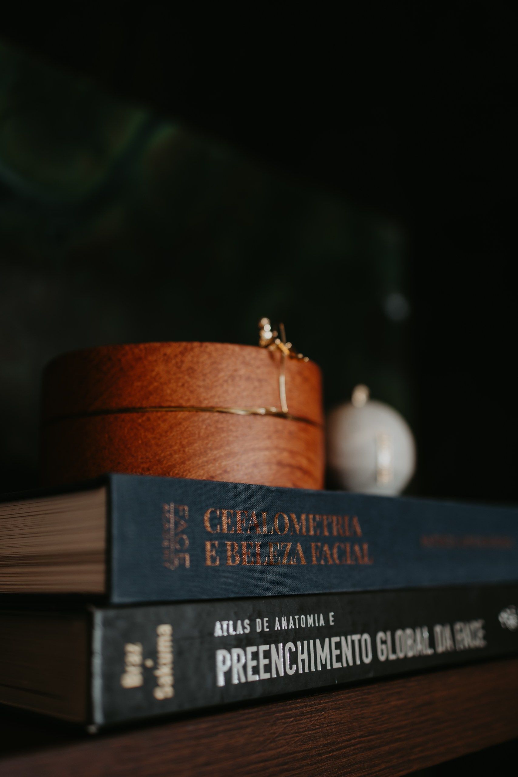 Pilha de livros com um chapéu de palha marrom em cima e um pequeno abajur ao fundo.