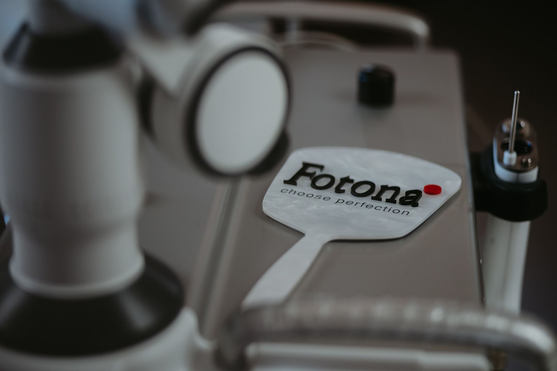 Detalhe do painel de controle de um dispositivo médico Fotona com placa de logotipo prateada e botões.