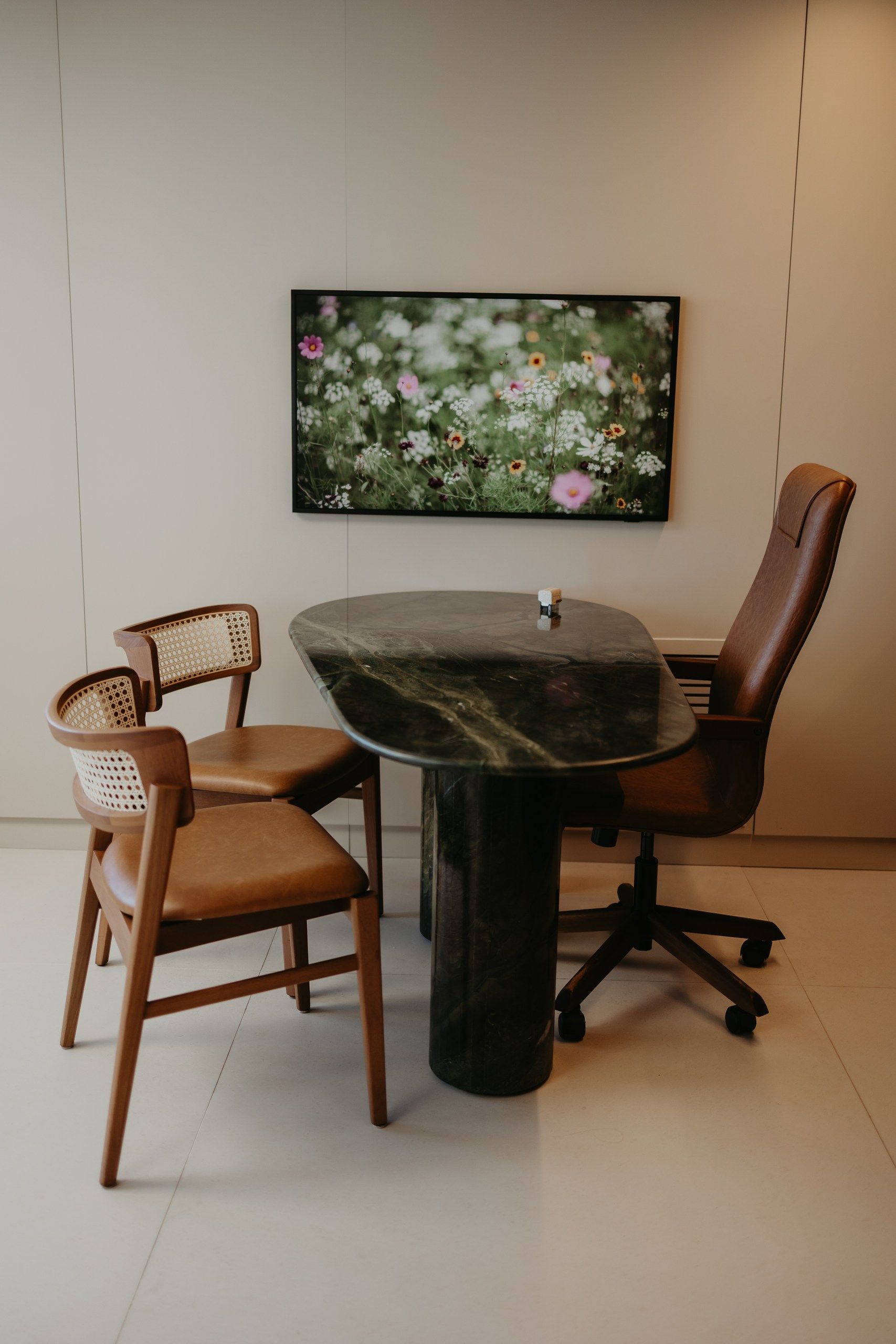 Pequeno recanto para refeições com duas cadeiras e uma mesa redonda escura sob uma gravura floral na parede.