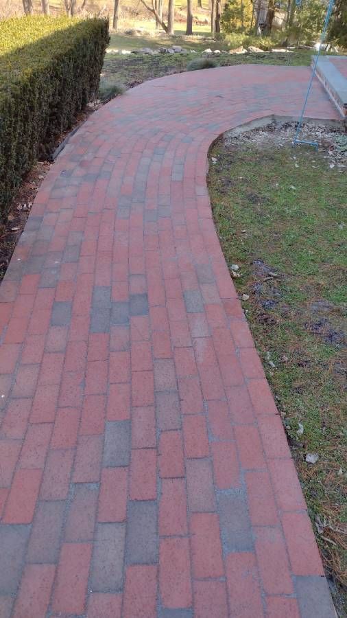 Curved red brick walkway beside a hedge and grass in a landscaped yard