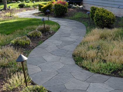 Curved stone garden path through landscaped grass and shrubs with small path lights