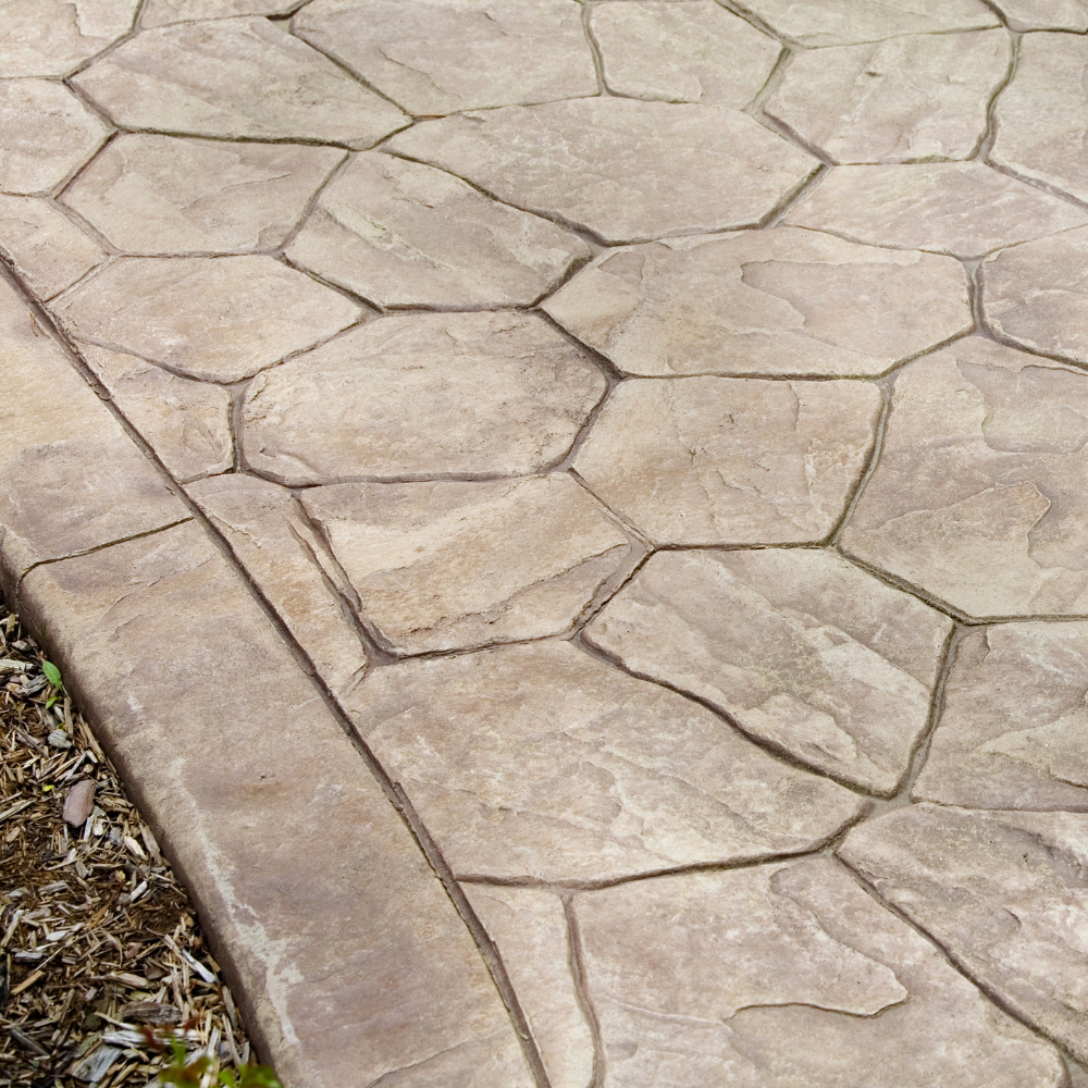 Stamped concrete patio with irregular stone pattern and curved edge bordering mulch