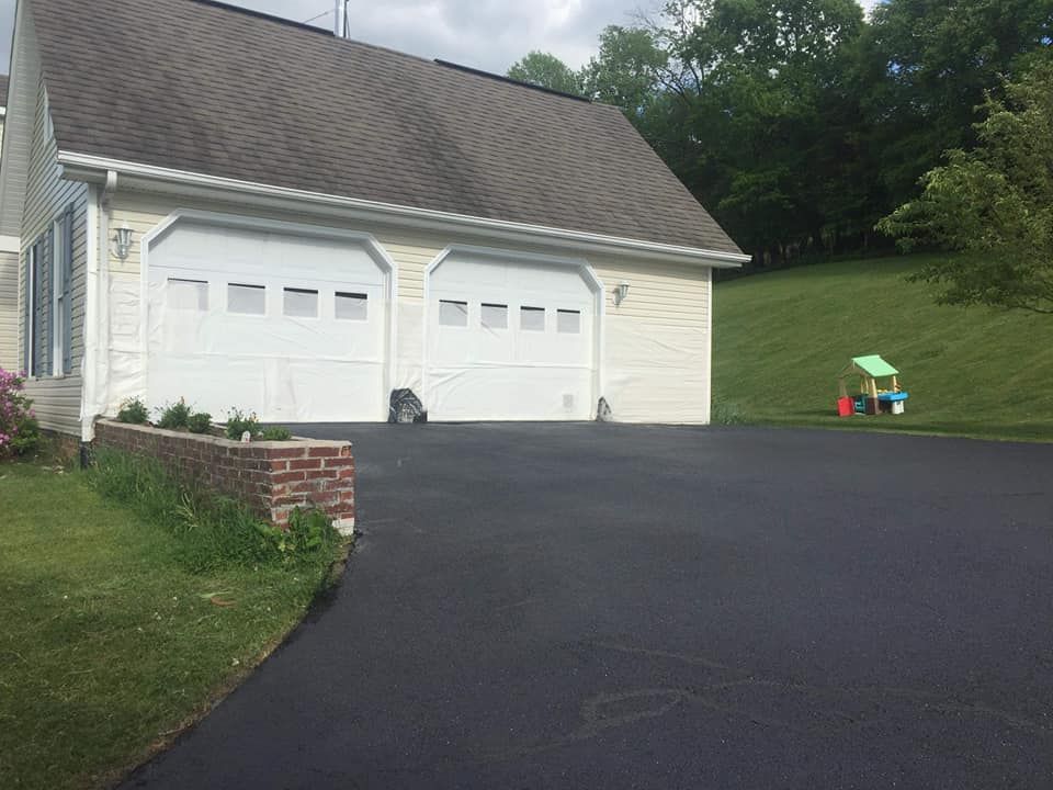 Black asphalt driveway leading to a two-car garage with white doors, surrounded by grass and a small playhouse.