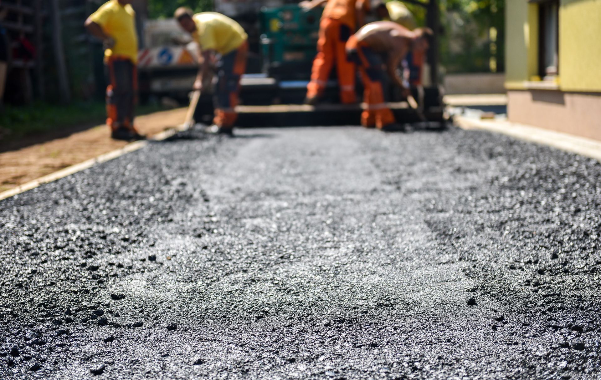 Crew laying and smoothing fresh asphalt on a residential driveway with paving equipment.