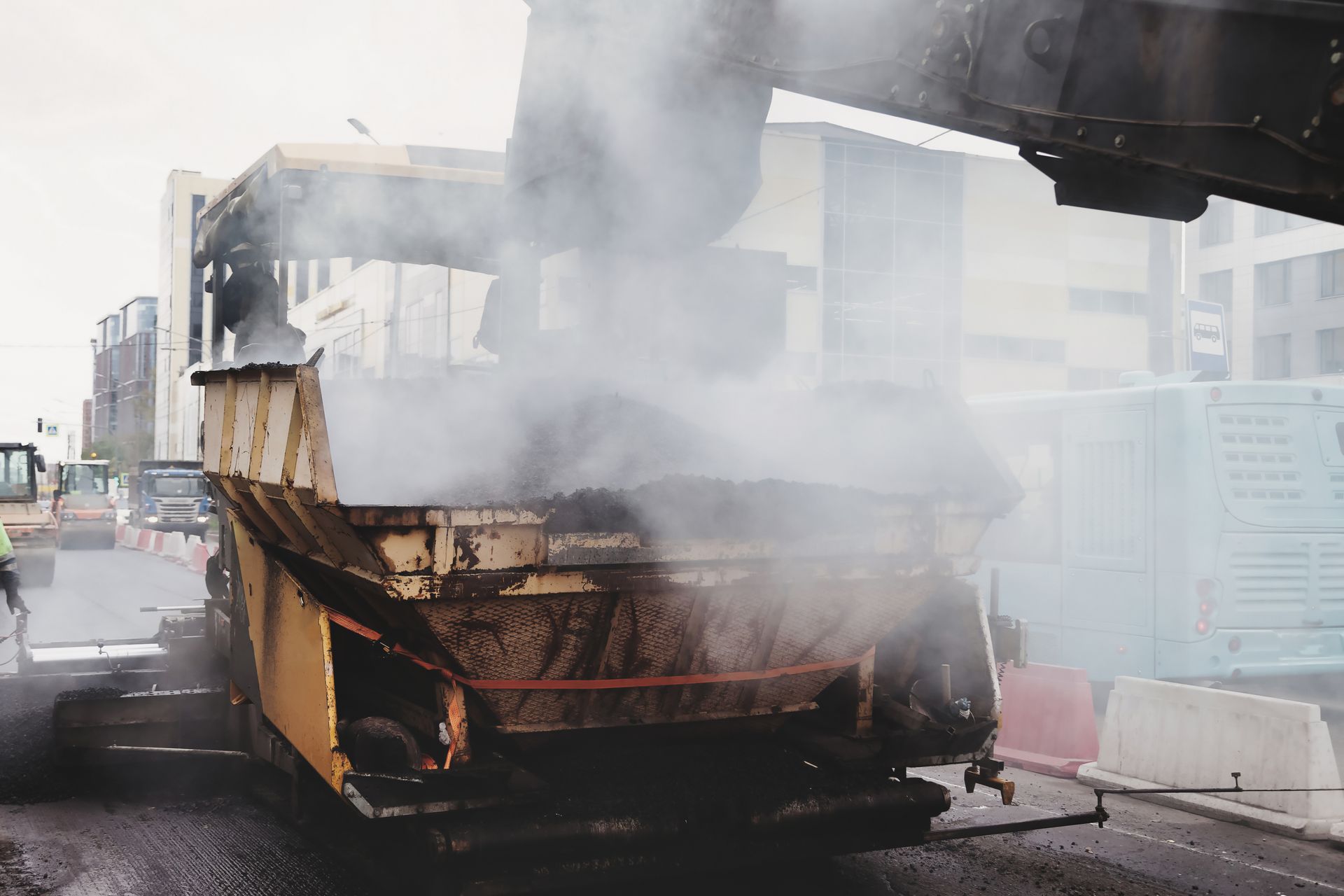 Workers are performing asphalt paving on busy streets.