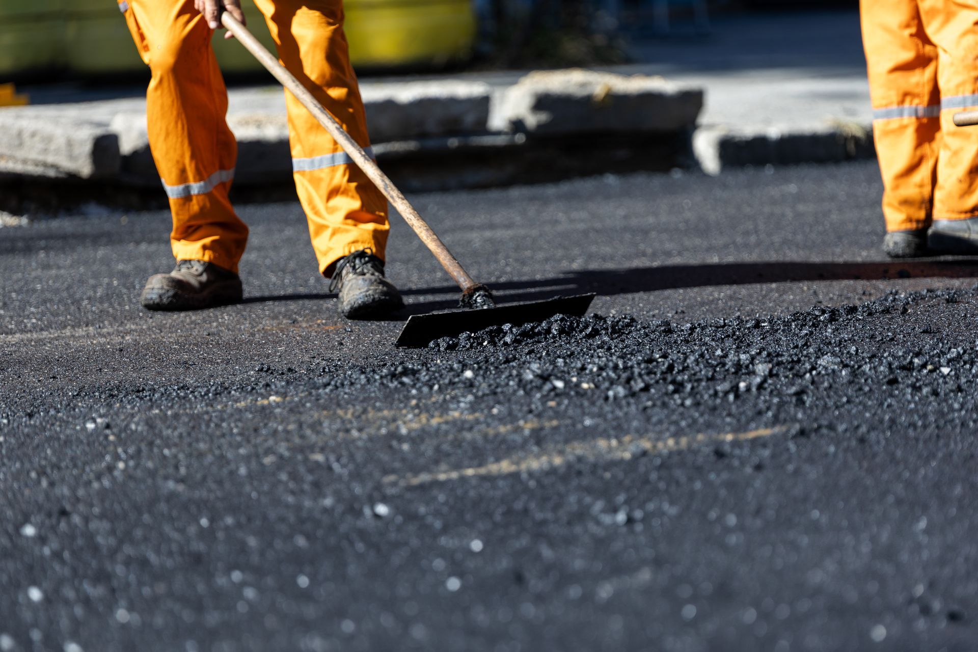 Road workers leveling fresh asphalt with a rake during paving work.