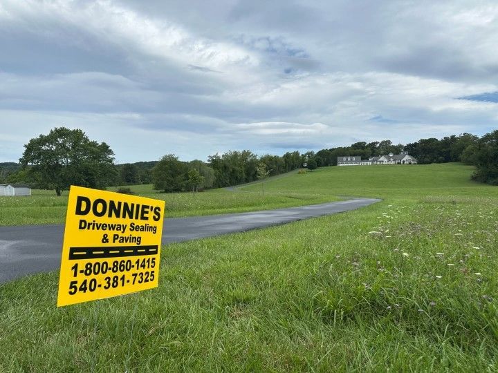 A yellow sign for donnie 's driveway sealing and paving is in the middle of a grassy field.