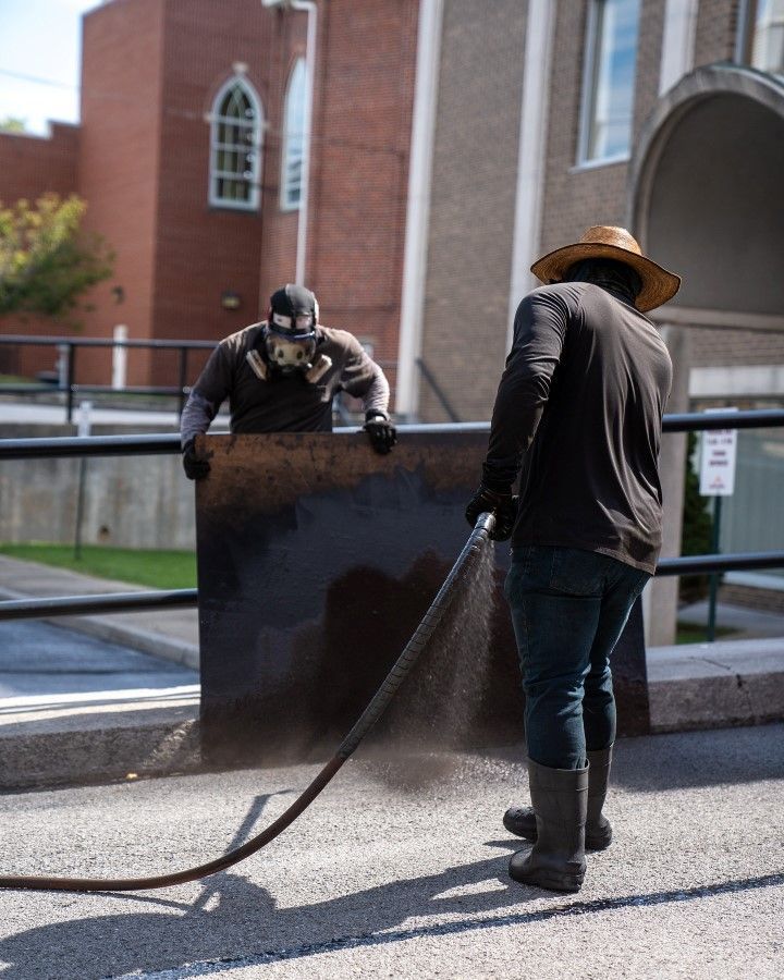 Two men are spraying a large piece of metal with a hose.