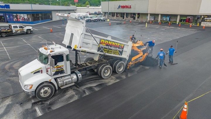 An aerial view of a dump truck spreading asphalt in a parking lot.