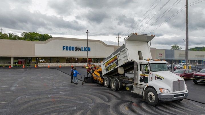 A dump truck is driving down a parking lot in front of a store.