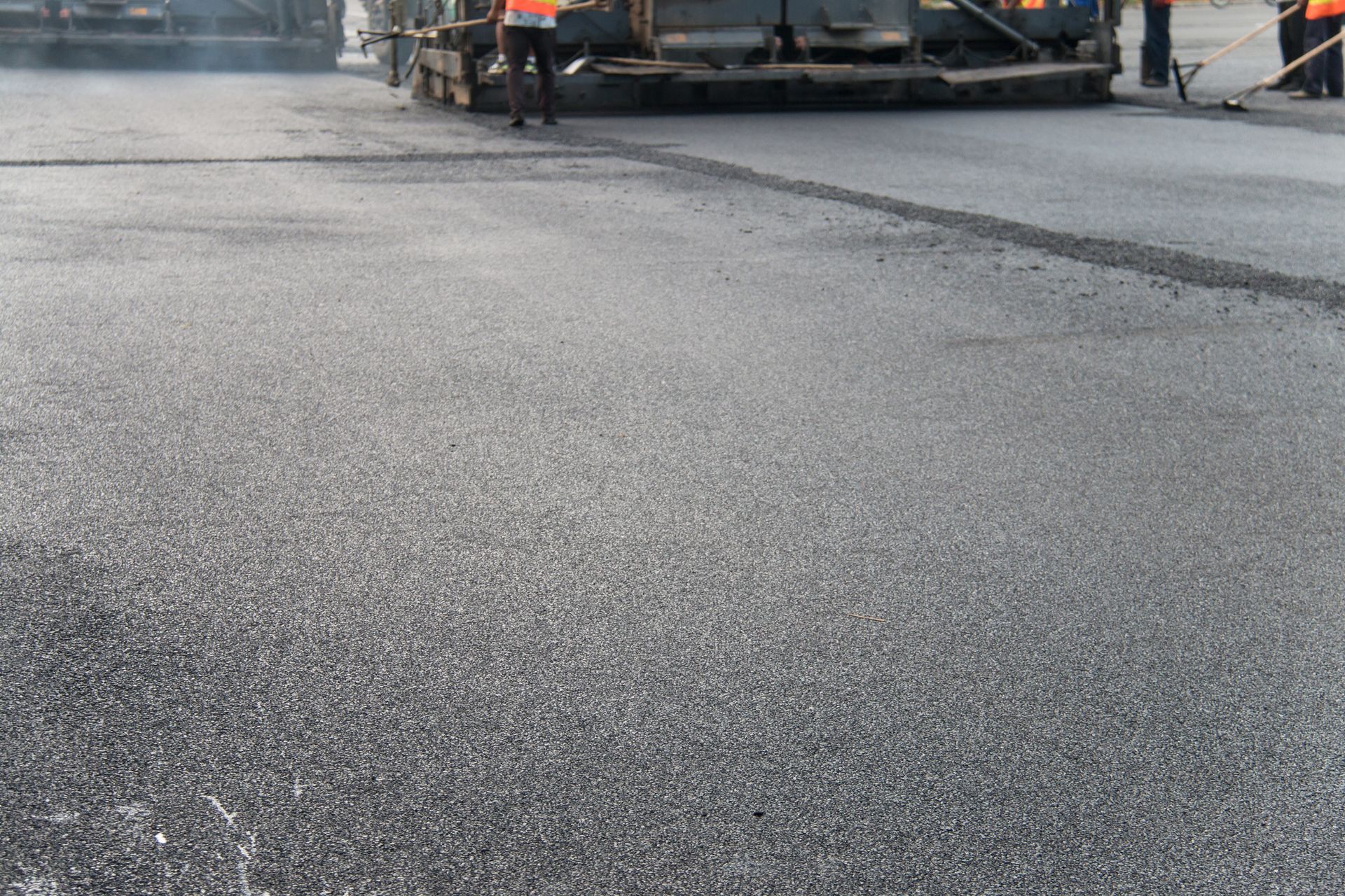 Fresh asphalt paving on road with construction workers and machinery during resurfacing work.