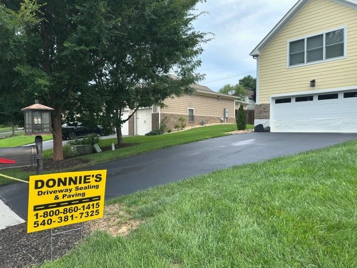 Freshly sealed asphalt driveway next to a grassy lawn with a yellow house and business sign.