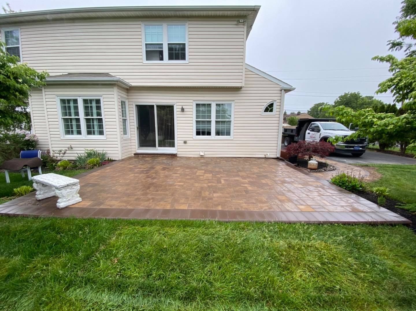 Backyard patio with brick pavers, house with siding, lawn, and a parked truck.