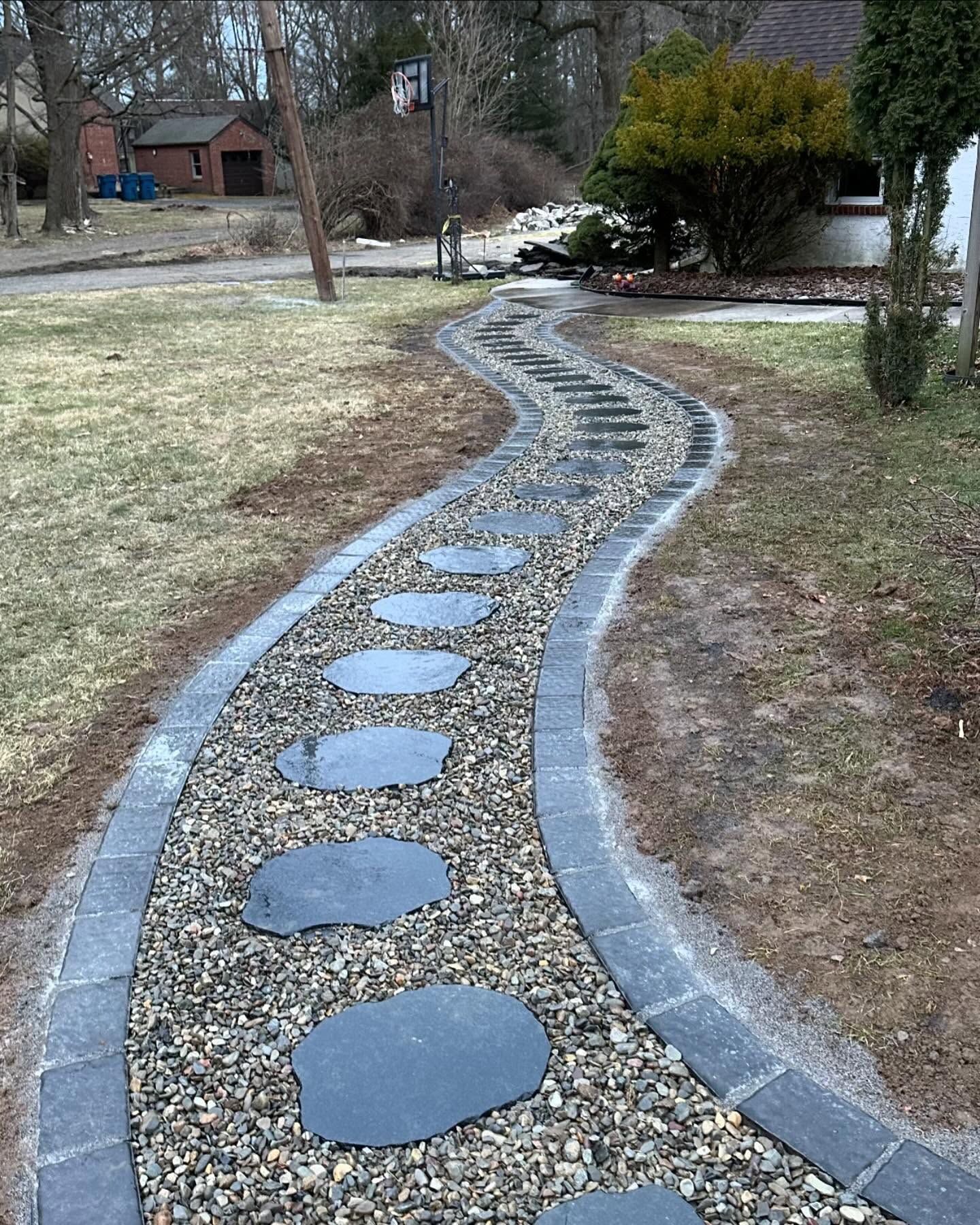 Stone path winding through a yard, with stepping stones, gravel, and border pavers.