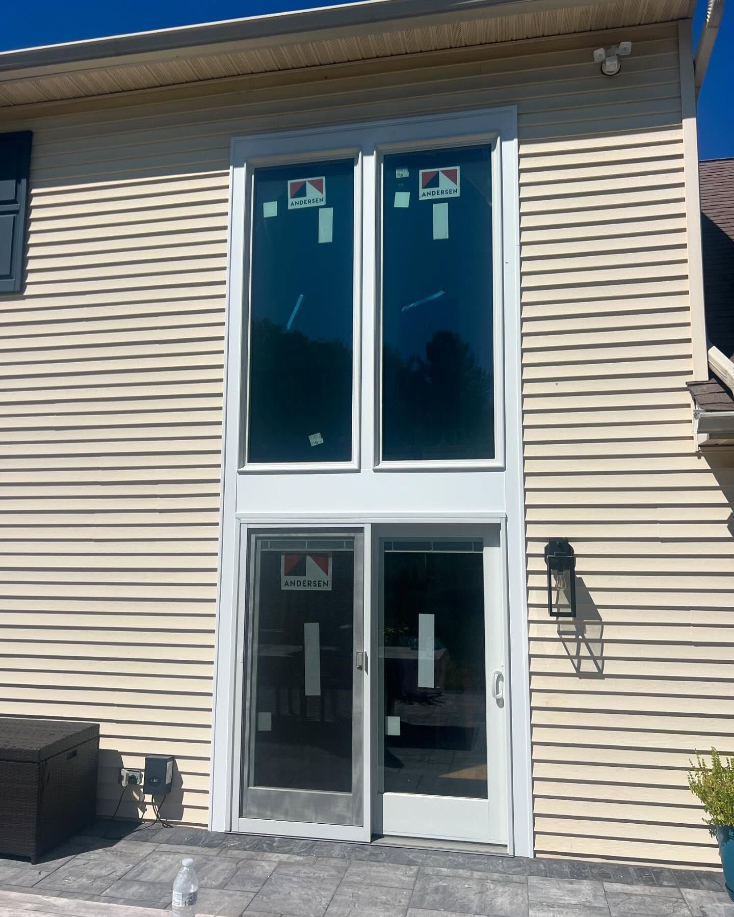 Two-story window and door combination in a beige building exterior with a light fixture on the right.