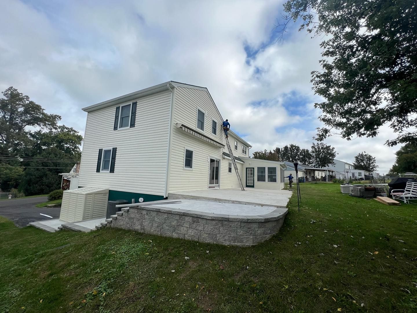 A two-story house with light-colored siding, a stone patio, and green grass on a cloudy day.