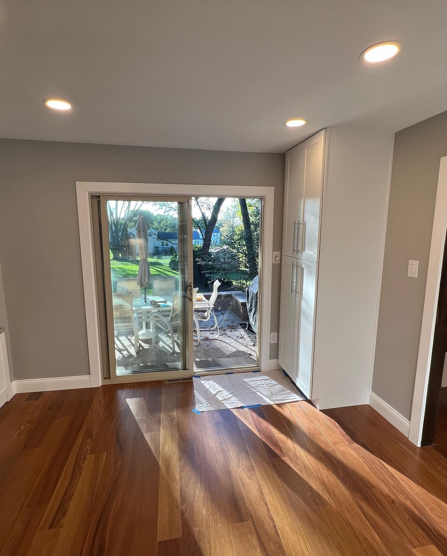 Wooden floor, sliding glass door to yard. White cabinets beside the door, gray walls, and recessed lights.
